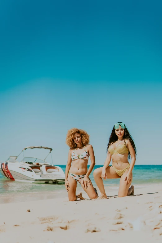 two pretty young ladies in bikinis sitting on the beach