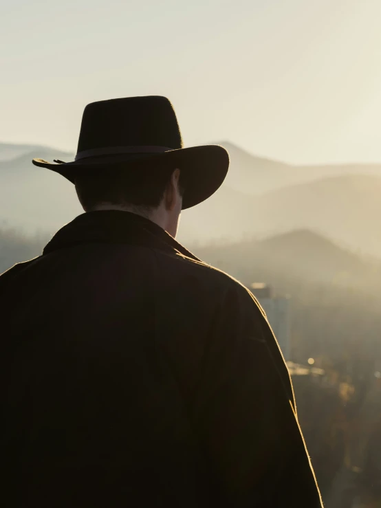 a man with a cowboy hat stares over mountains