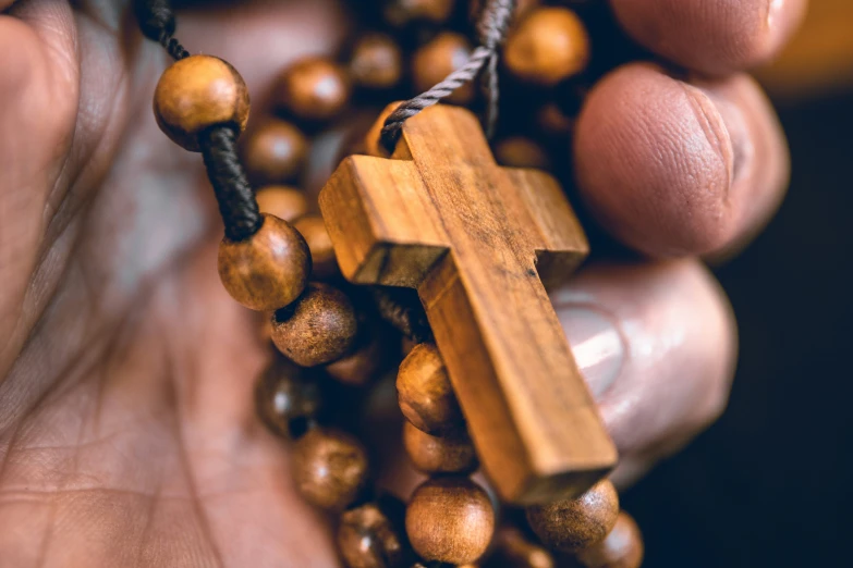 the person is holding a cross shaped wooden bead