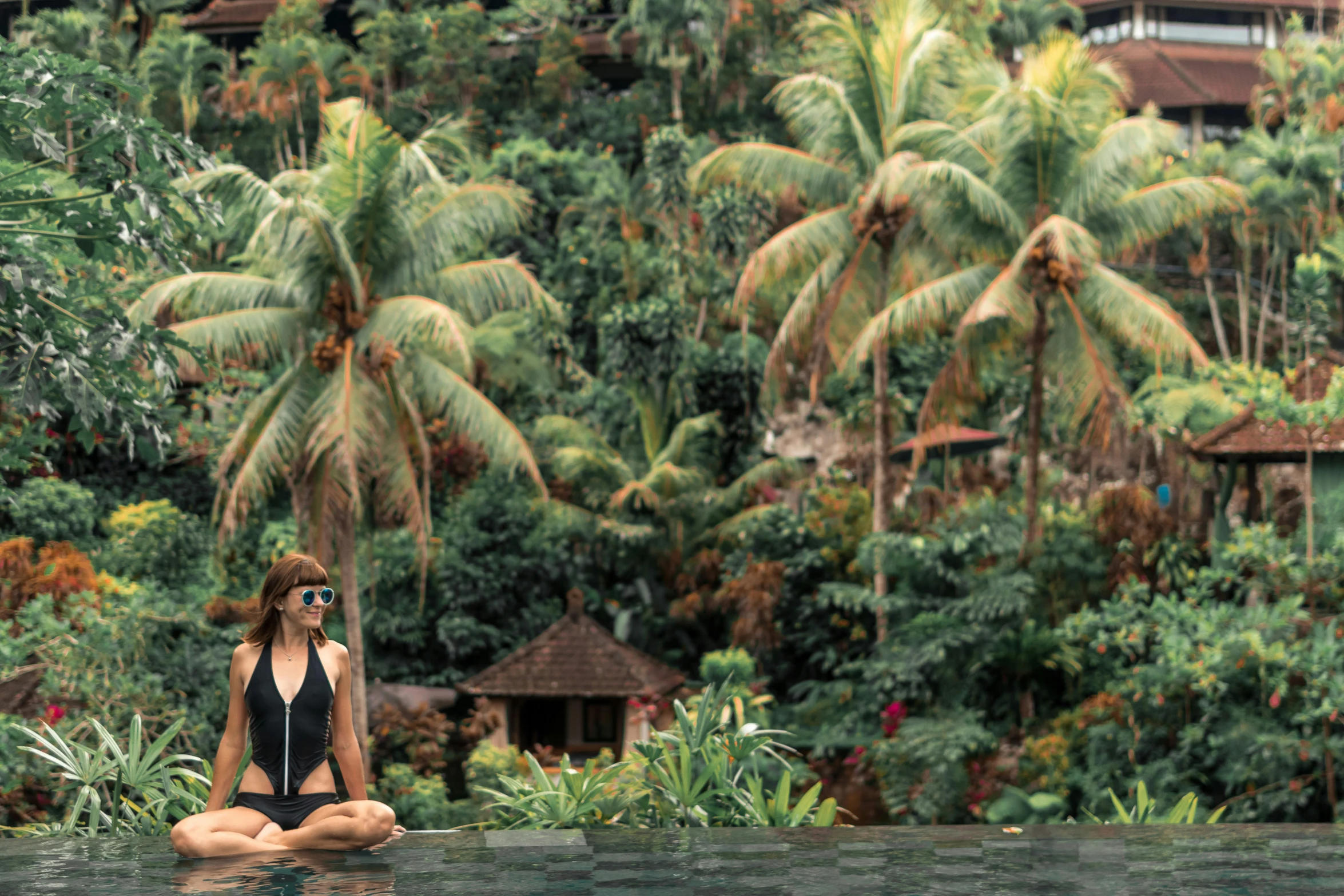 a woman sitting on a body of water wearing a black swimsuit