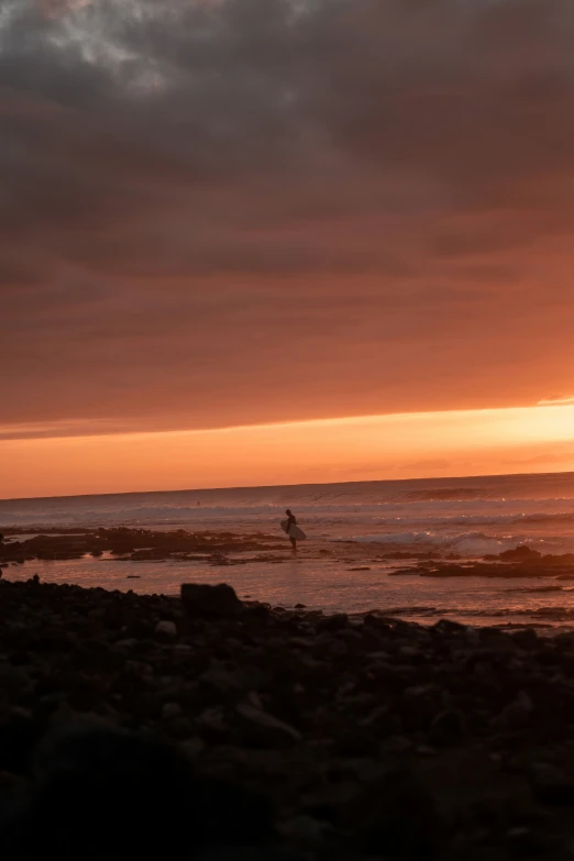 the surf boarder walks through water while the sun sets