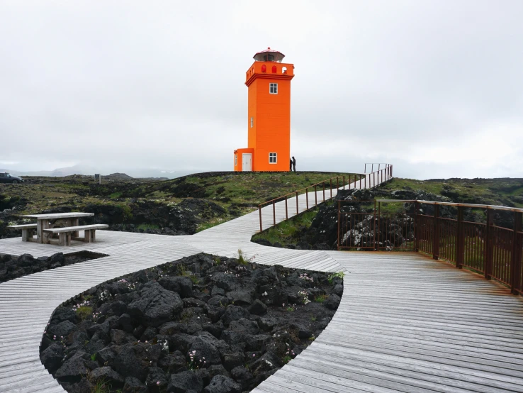 a wooden walkway leads to a bright orange tower