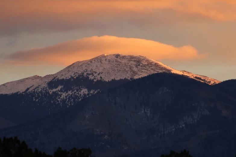 a mountain range with trees in front of a sunset