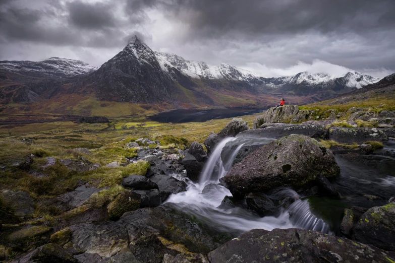 a man stands on rocks by a small waterfall