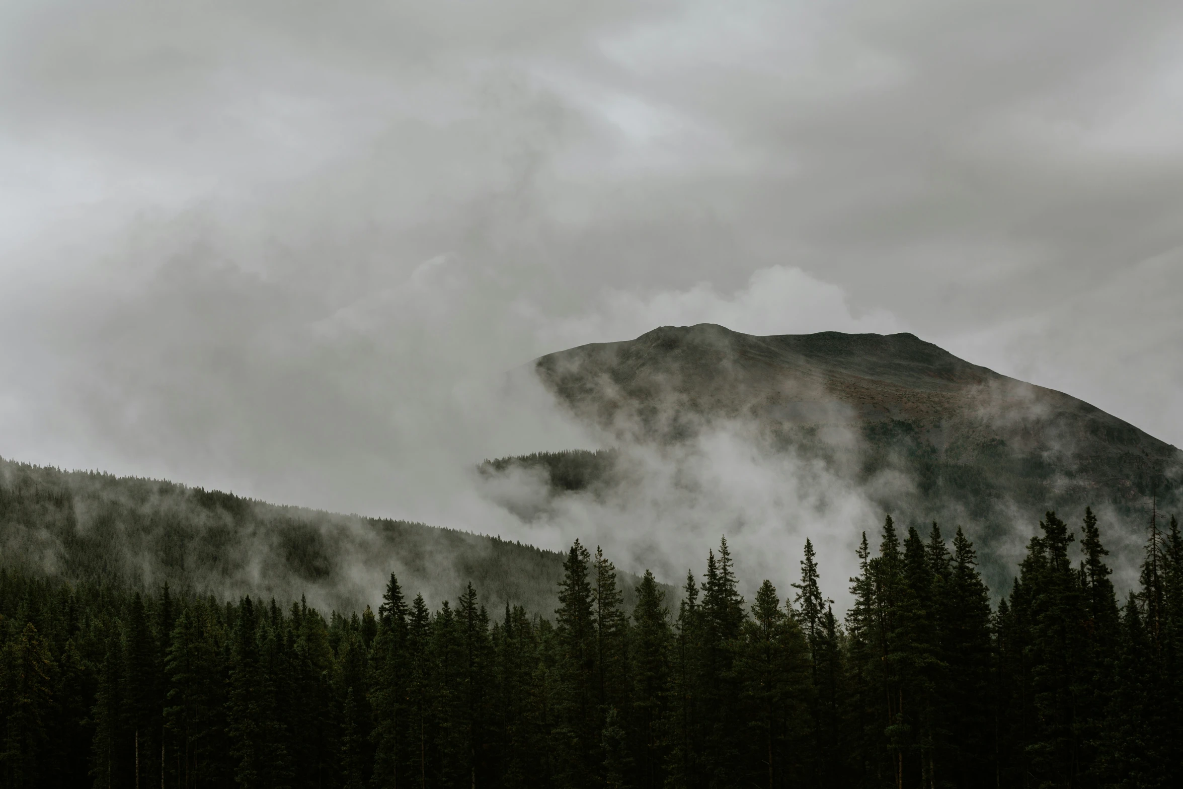 mountains covered in smoke and fog under cloudy skies