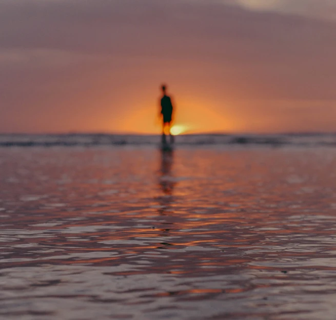 two people stand in the distance on the beach at sunset