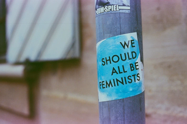 a sticker on a blue pole with we should all be feminist