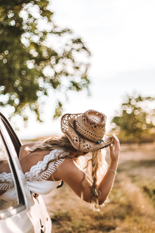 a woman holding her hat and standing near the side of a car