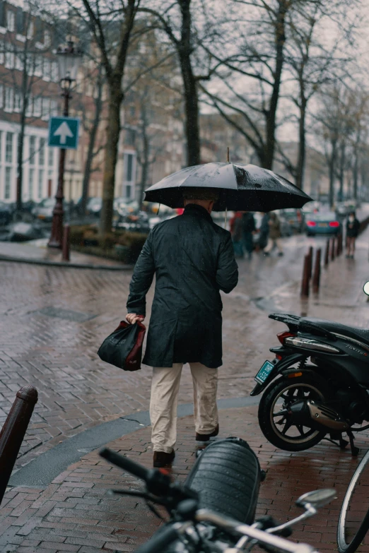 a man walking on a wet sidewalk with a black umbrella