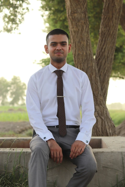 a man sitting on cement in a dress shirt and tie