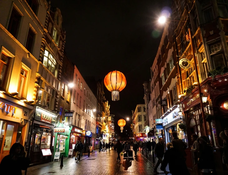 people walking along a street at night with hanging lanterns