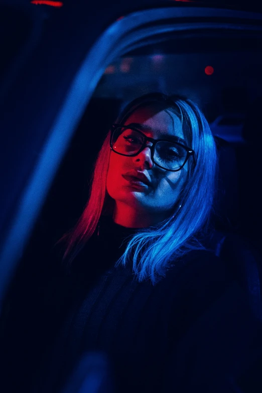 a woman wearing glasses sitting in a car with the door open