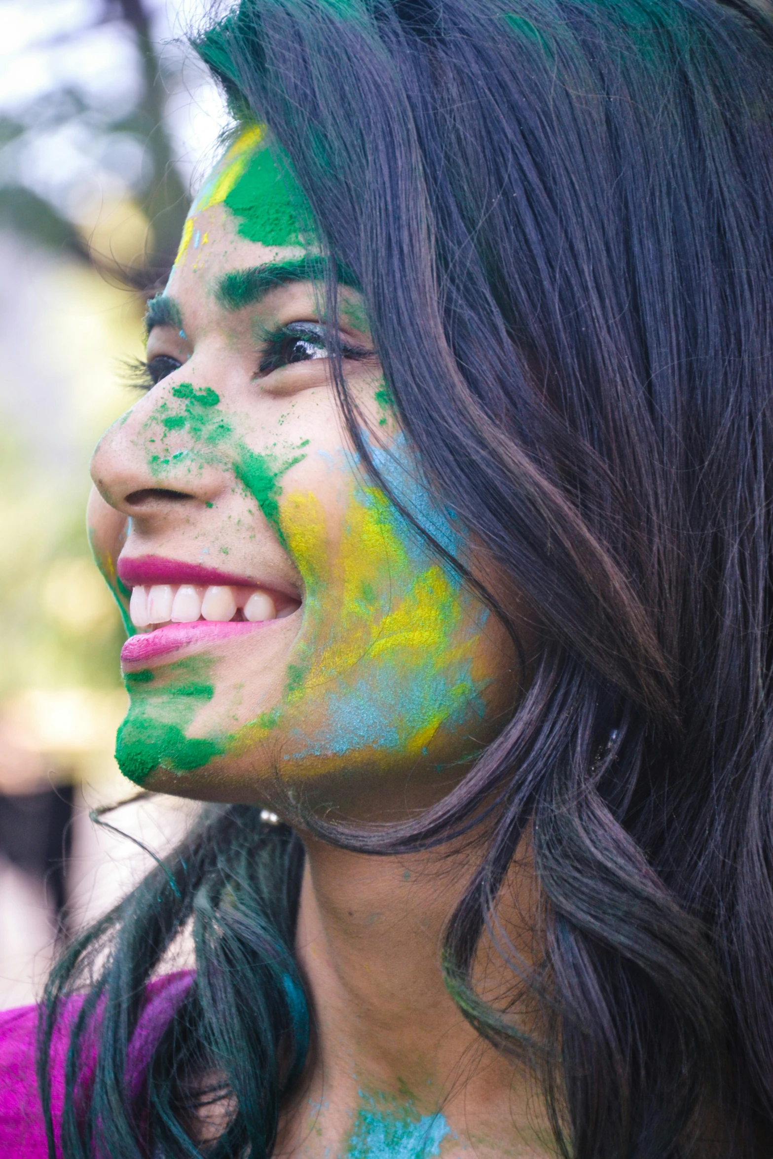 a girl with her eyes closed smiles while her face painted bright green and blue