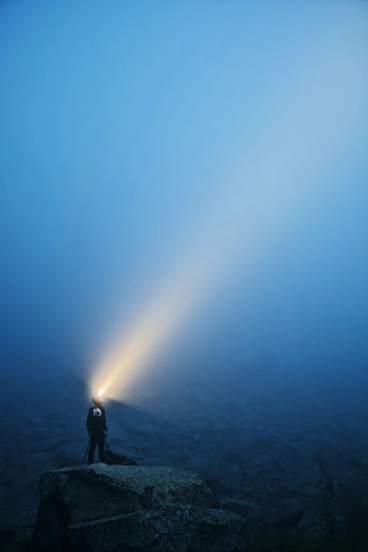 man standing on a cliff with a light from his head