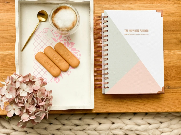 a plate with food, a cup, a bowl, and spoon next to a notebook on top