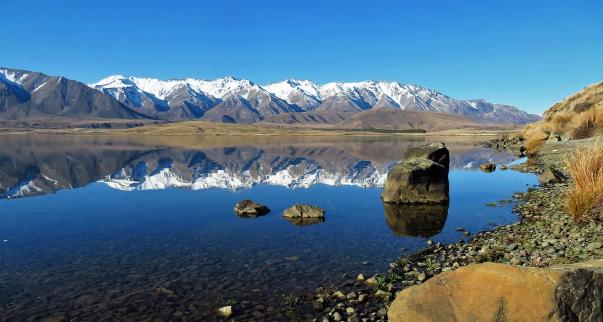 a mountain range with snow on top of it and a body of water in the foreground