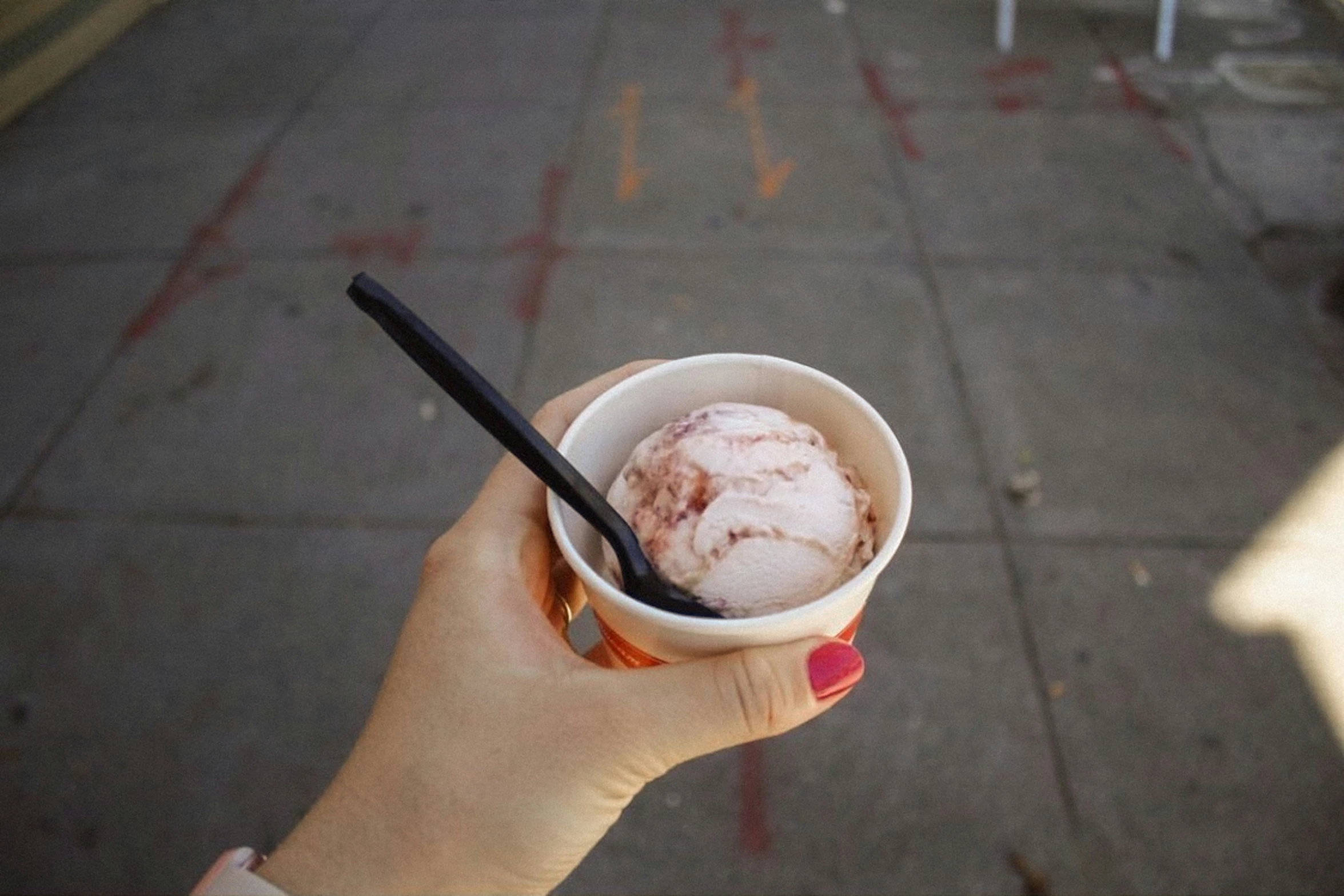 a hand holding a cup of ice cream on a sidewalk