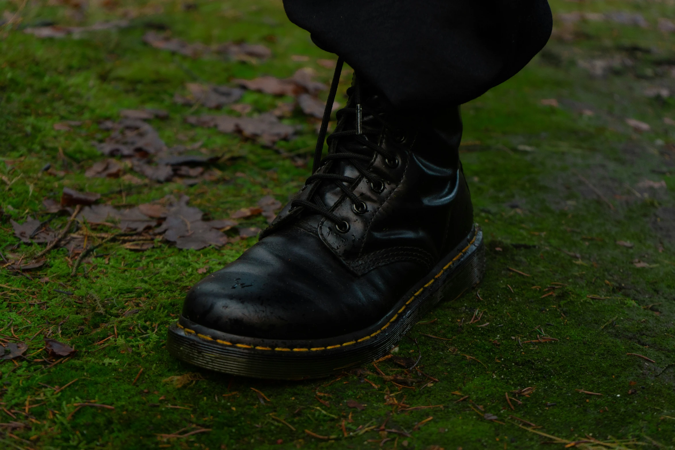 person in black dress boots and boots walking around in the grass