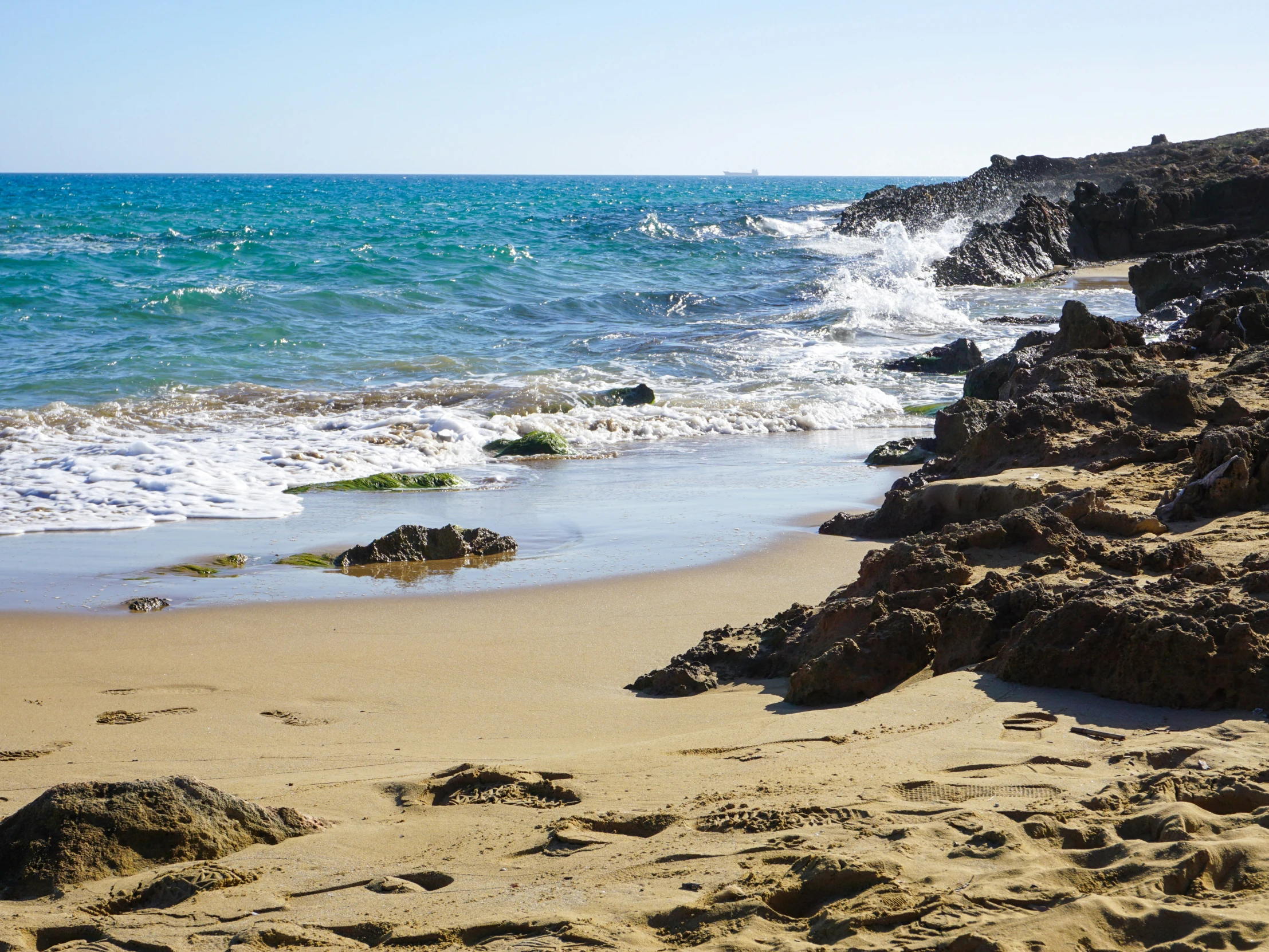 waves hitting shore line on sandy beach next to rocky shoreline