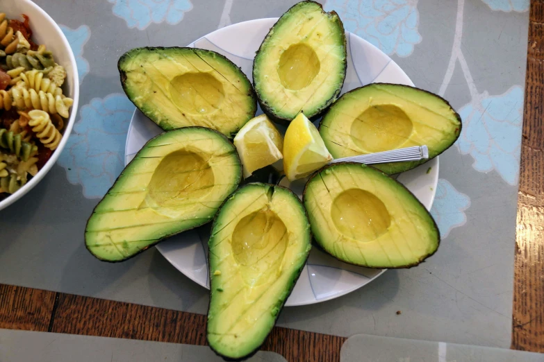 an avocado cut in half sitting on a white plate next to a bowl of pasta