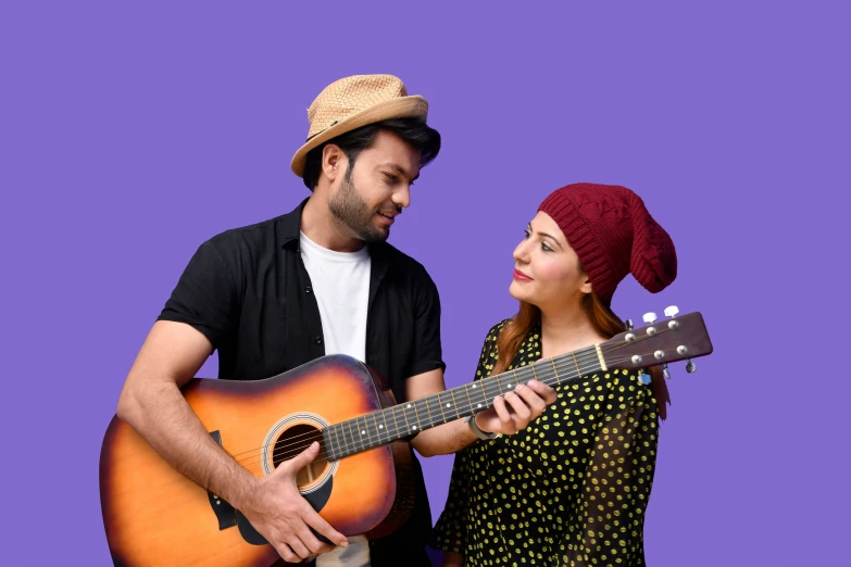 a woman and man standing in front of a purple background holding a guitar