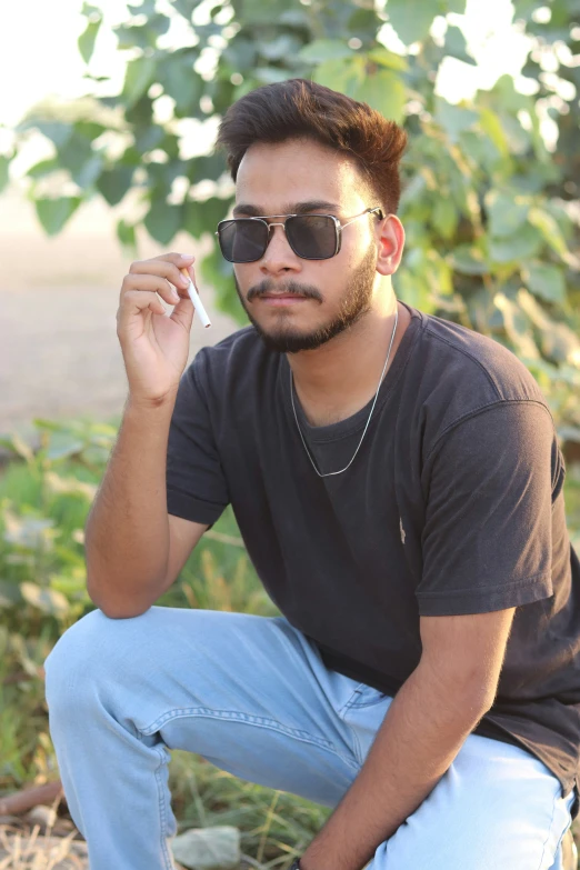 a man sitting in front of a bush while holding a cigarette