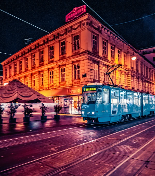 a blue trolley on a track going past a tall building