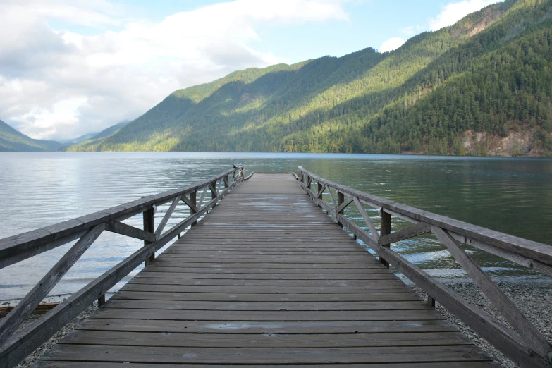 a pier is on the side of a lake with hills in the background