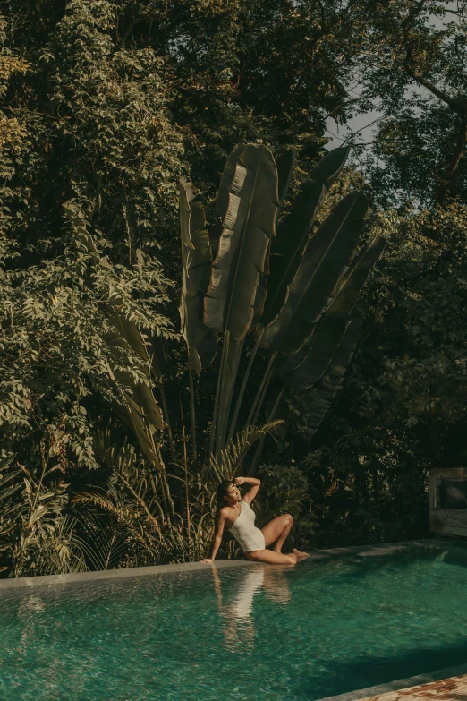 a woman sitting next to a pool next to some trees
