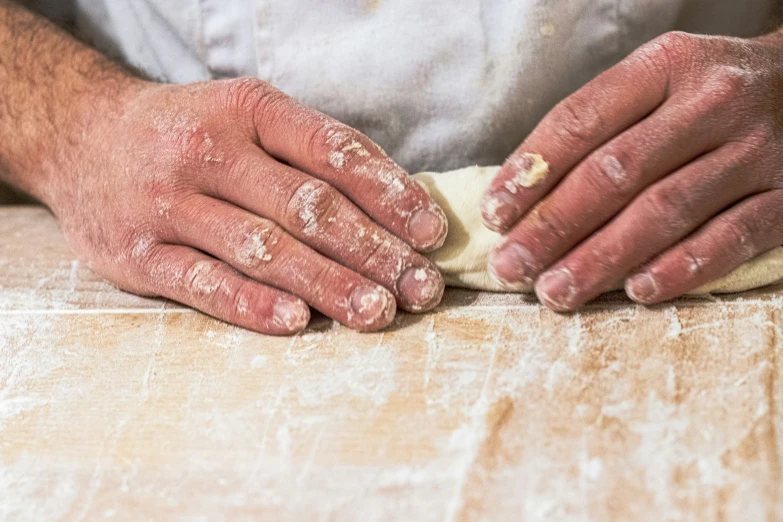 a man with a white apron and gloves on making dough