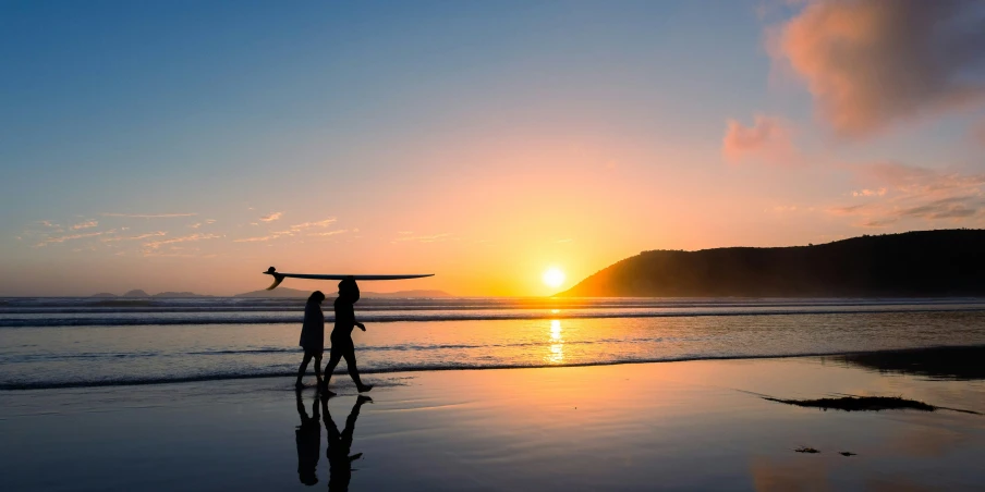 two surfers stand at the end of their surfboards as the sun rises over the ocean