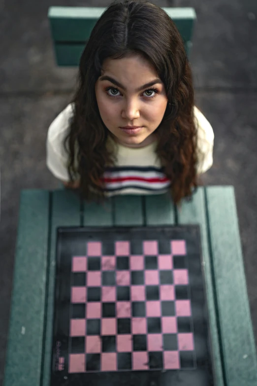 a woman with brown hair is sitting in a bench with a checker board on it