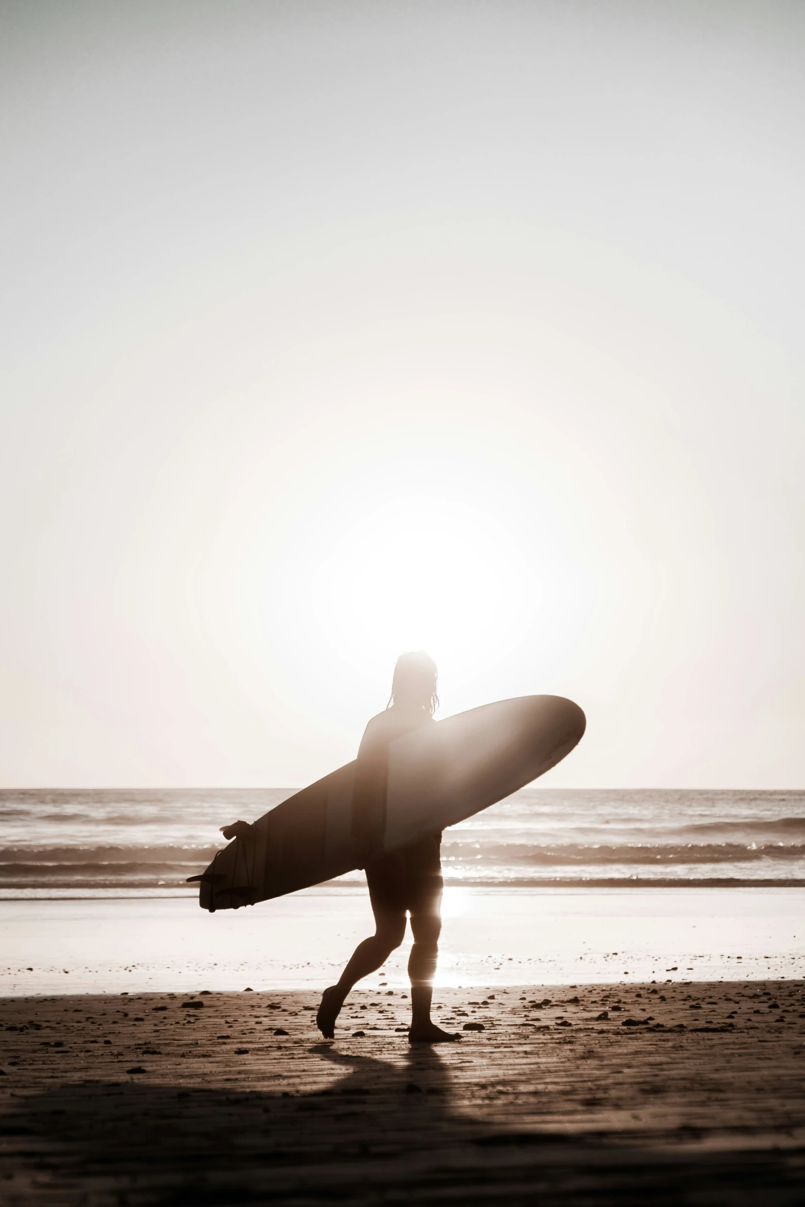 silhouette of person carrying surf board on beach in sunshine