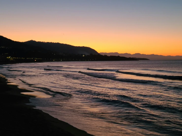 sunset on a beach with ocean and mountains in the background