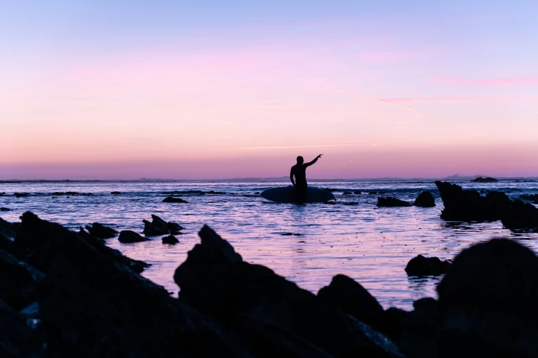 a man standing on a rock in the ocean at sunset