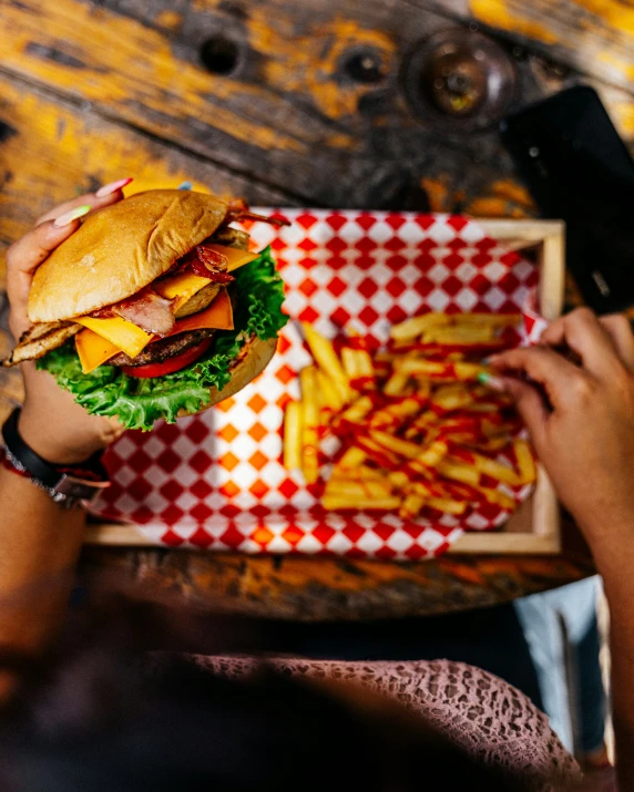 two people holding a large cheeseburger and french fries