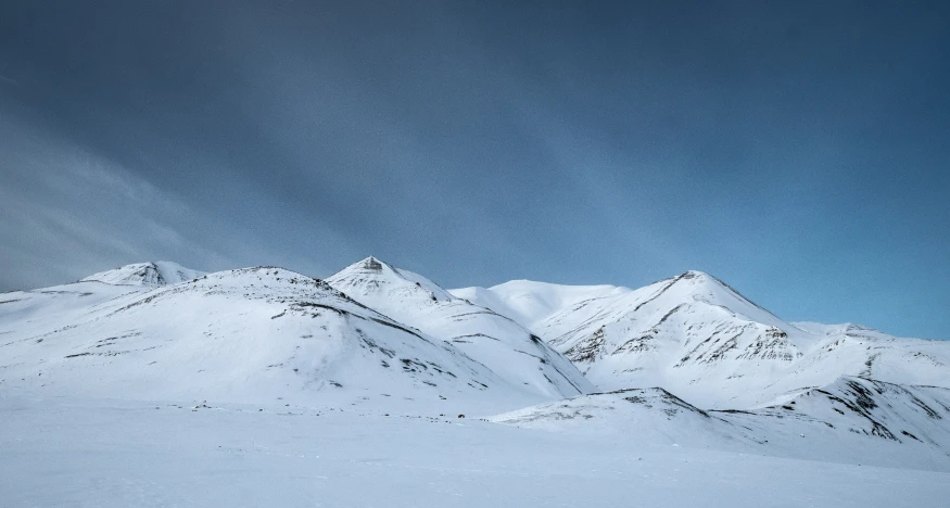 a large snow covered mountain range under blue skies