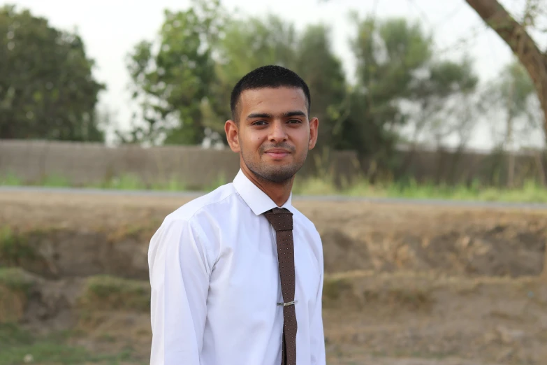 the man wearing a neck tie stands near a dry field