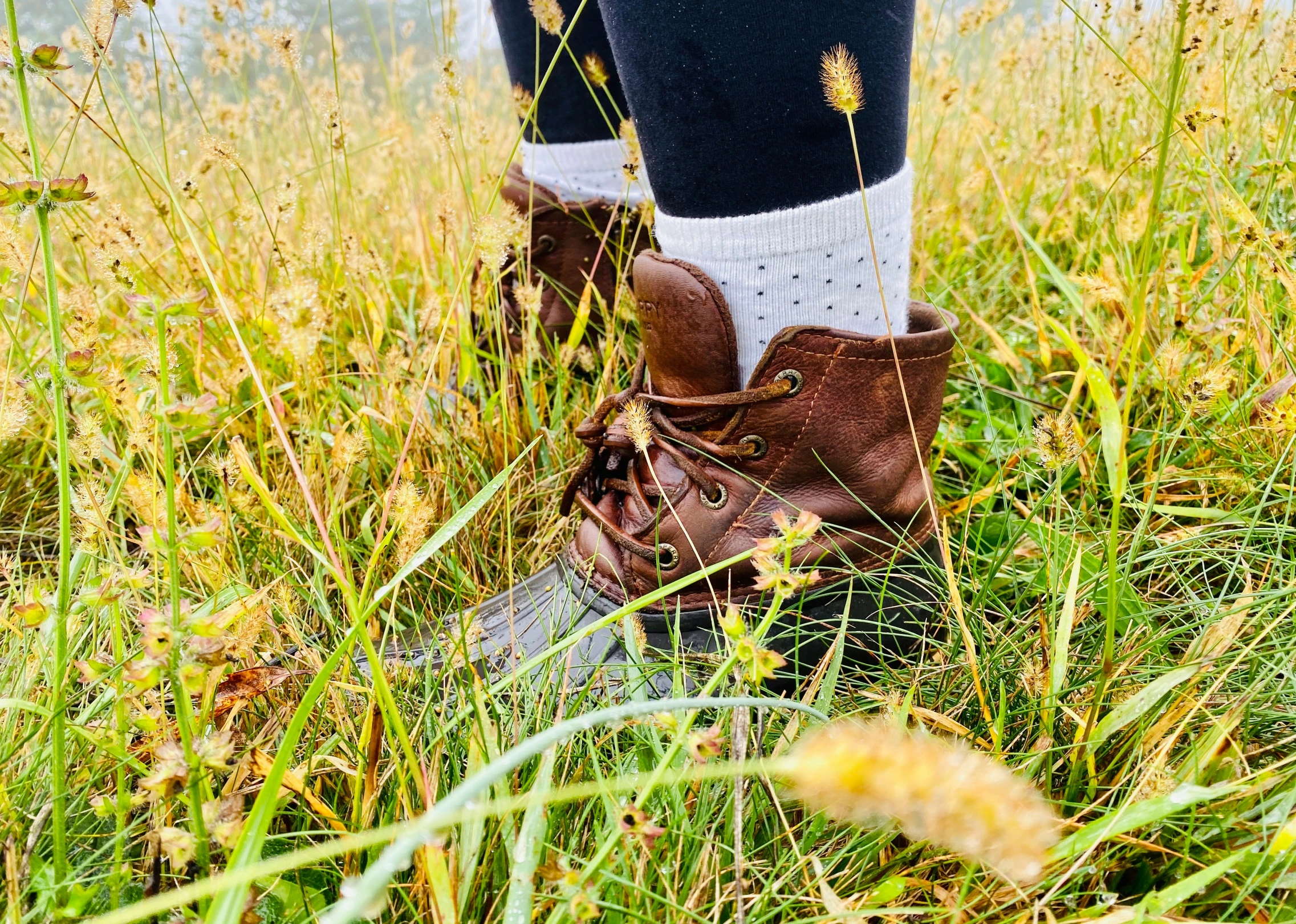 a person wearing socks and boots standing in the grass