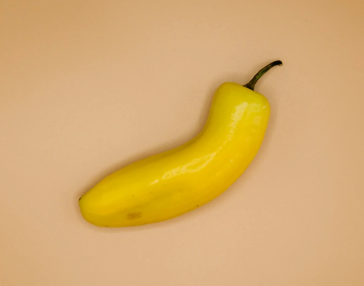 a single yellow banana is pictured against a brown background