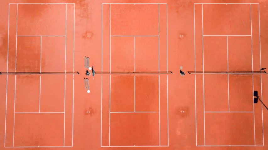 two people are holding rackets in their hands standing on an orange tennis court