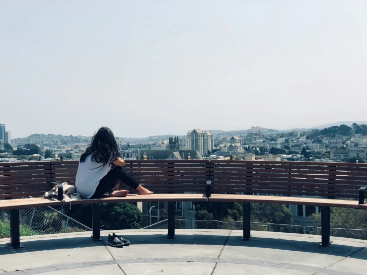 a woman sitting on a bench in front of a city