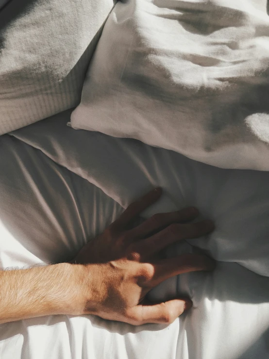 hand extending out on an unmade bed with sheets