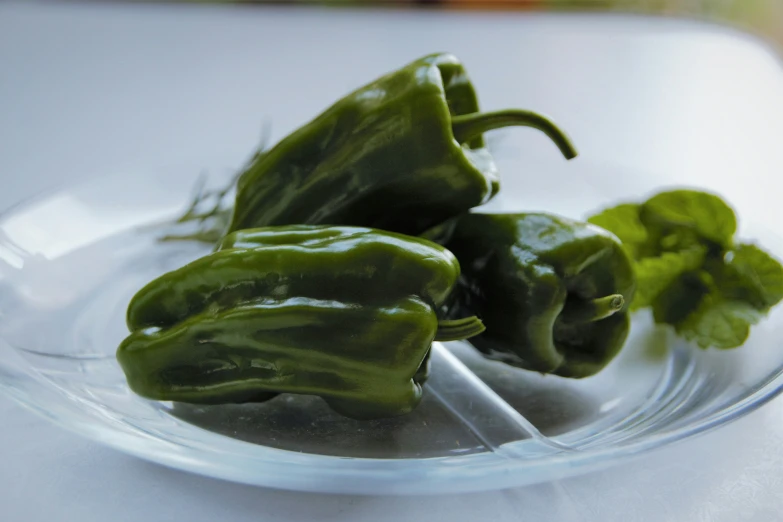 three green peppers in a glass dish next to a silver spoon