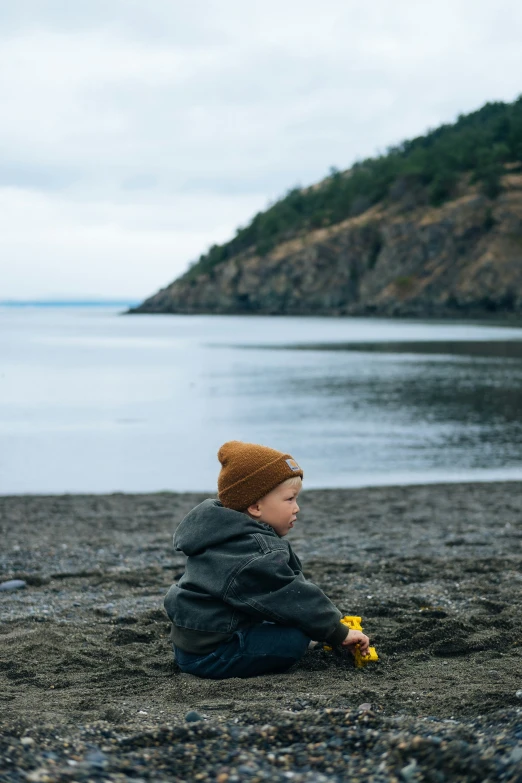  wearing hat sitting on beach with ocean and rocky shore