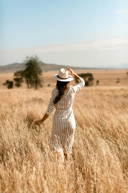 a young woman stands in the middle of a field, while wearing a white hat