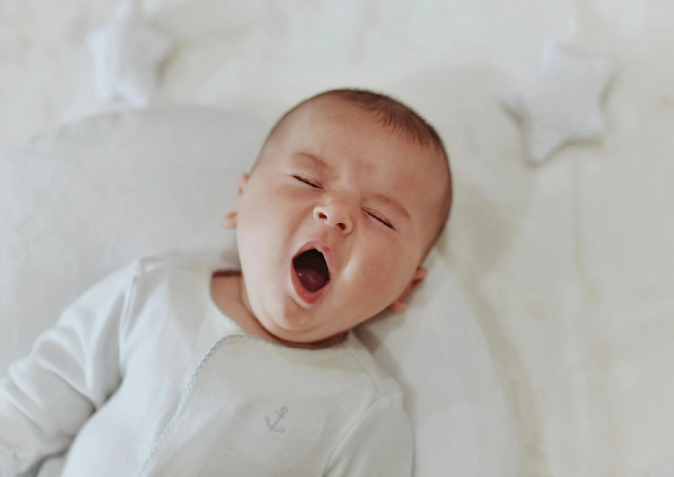 baby laying down while yawning on a blanket