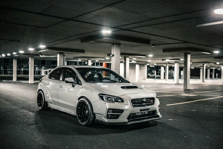 a white subaru wrx on 22's is parked inside a parking lot