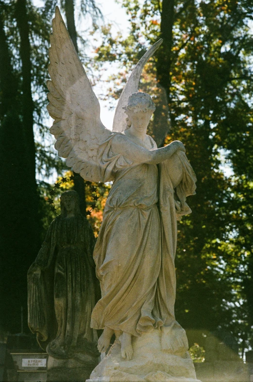 the statue of an angel stands outside by the trees