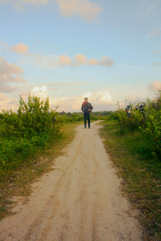 a man walking down a dirt road towards a blue sky